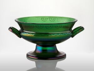  A translucent green glass bowl with decorative etching on the rim and two stylized handles, mounted on a dark green pedestal base. Artist name and title are unknown.