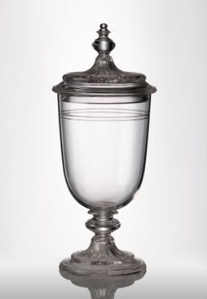  A transparent glass chalice with a cover, featuring a smooth, rounded bowl, an adorned rim, and a decorative finial on the lid, displayed against a light grey gradient background.