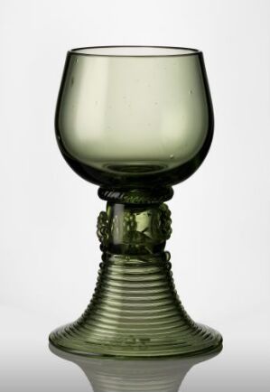  An antique green glass goblet with intricate details on the stem and ridged base, set against a gradient background transitioning from white to light gray.