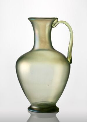  A subtly green-tinted translucent glass pitcher with an elegant design, featuring a bulging center, a shapely neck, and a gracefully curved handle against a clear background. Artist name and title are unknown.