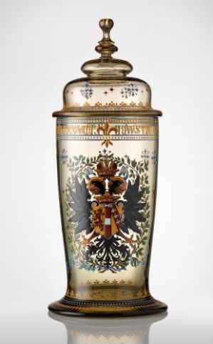  An ornate cylindrical cream-colored vessel with a lid, featuring a detailed coat of arms and golden accents against a neutral background. Artist name and title unknown.