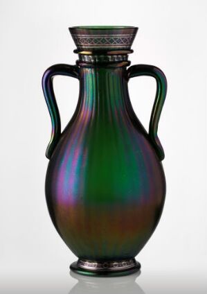  An iridescent glass vase with a multicolored sheen, featuring a flared opening, ridged decorative band around the neck, and two symmetrical handles attached from the neck to the body of the vase, all against a light gray background. Artist name and title unknown.