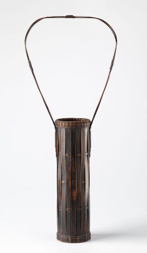  A cylindrical dark brown object with lighter vertical streaks and a dull metallic wire handle against a white background. Artist and title are unknown.