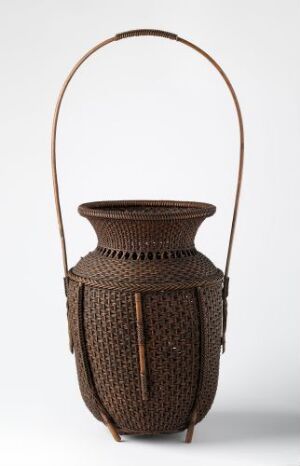  A handcrafted woven basket with a sturdy arched handle and intricate designs, colored in natural shades of brown against a neutral light gray background.