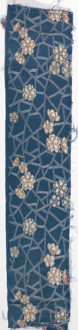  A long, narrow strip of dark blue fabric featuring a repeating pattern of intricate floral motifs in white, beige, grey, and light blue, arranged in a scattered fashion against a faint crisscrossing lattice design.