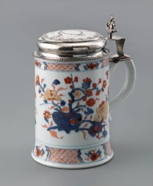  A decorative ceramic beer stein with a white background and a floral pattern in blue, orange, and green, completed with a pewter lid and handle.