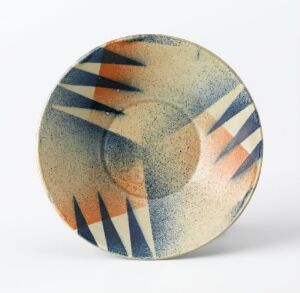  A round ceramic plate by Egersunds Fayancefabrik with a cream and pale blue mottled background, adorned with orange arches and black geometric patterns.