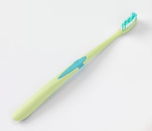  A pastel yellow-green toothbrush with a turquoise blue grip and multi-colored bristles designed by Jordan A/S, lying on a white background, showcasing its sleek design and ergonomic features.