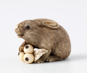  A realistic brown rabbit figurine in a crouched position, with detailed fur texture, holding three nut-like objects with carved leaf patterns against a light grey background. Artist and title unknown.