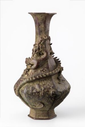  An ornate, antique-looking vase with a bulbous body and slender neck, decorated with intricate three-dimensional designs, standing against a light background.