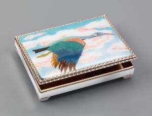  A small, decorative box with an artistically rendered bird in flight on the lid, showcasing vibrant blues, greens, and oranges against a soft blue and white cloudy sky background, set on a light gray surface.