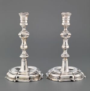  "To lysestaker" by Jonas Sørensen - a pair of crafted silver candlesticks with engraved designs, set against a simple grey background, showcasing the shimmering surface and ornate details of the pieces.