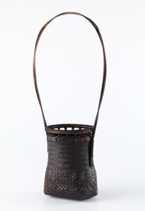  A traditional dark brown woven basket with a handle, featuring a fine, intricate weave pattern and a series of small openings around the top edge, set against a solid white background.