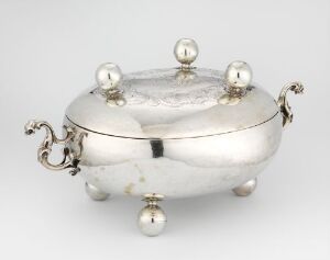  A polished silver oval-shaped tureen with a lid, featuring four spherical legs and decorative scrolled handles, displayed against a white background.