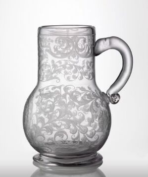  A translucent glass pitcher with intricate floral etched design on a plain gray background.