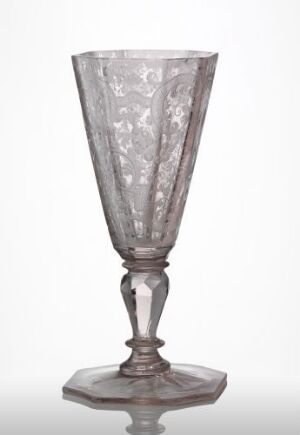  An antique-looking, transparent glass with a conical bowl, a faceted stem, and a rounded base, featuring a detailed etched floral pattern, set against a soft white background.