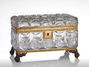  A decorative chest made of clear patterned glass with a gold-colored ornate band and pawed feet, suggestive of elegant antique furniture.