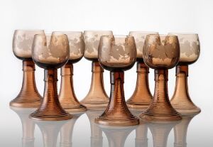  A set of seven symmetrical goblets with chalice-shaped cups in cream and brown tones, featuring an organic, flowy texture, placed on a reflective surface against a soft white-to-gray gradient background.