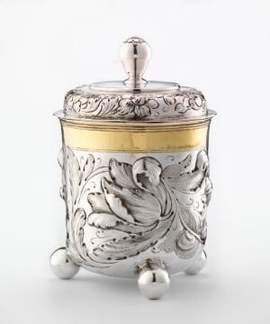  Silver tableware item, titled "Beger" by Hans d.e. Nieman, displaying embossed floral and leaf patterns, with a gilded central band, and three small spherical feet, representing exquisite silver craftsmanship with gold detailing.