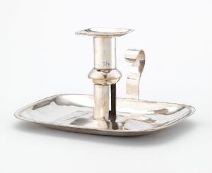  A silver candlestick holder with an attached handle is placed on an oval tray, both exhibiting a polished, reflective finish on a pale neutral background. Artistname and title are unknown.