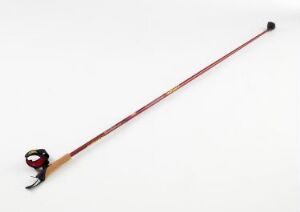  A Swix Sport AS ski pole with a burgundy to pink gradient on the shaft, a dark brown and gold ergonomic grip with a colorful strap, and a black snow basket, set diagonally against a light-colored background.