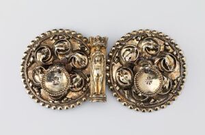  An intricate, golden-toned, symmetrical metal object with filigree designs and a central hinge, likely a piece of antique jewelry or decorative hardware, set against a light gray background. Artist name and title are unknown.