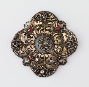  A traditional Norwegian "Beltesølje" intricately crafted in dappled silver with chasing and gilding techniques, featuring circular and floral-like motifs with deep red polished glass stones set into the metal, displayed against a neutral background. Artist unknown.