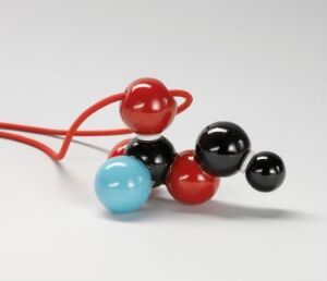  "Molecular Cluster 1," a jewelry design by Kirsti Reinsborg Grov, featuring a cluster of glossy enamel beads in vibrant red, sky blue, and reflective black on a flexible red rubber thread, resembling a structure of interconnected molecules.