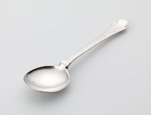  A silver spoon known as 'Spiseskje' by Carsten Lauritzen, with a reflective surface, rests on a light grey background. The spoon features an elegant design with a broad, oval bowl and an engraved handle, exemplifying traditional silver-making techniques and intended for table use.