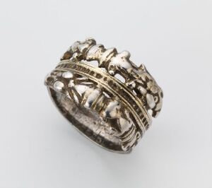  A silver-colored, intricately designed ring with a crown-like motif and textured bands, set against a white background. Artistname and title unknown.