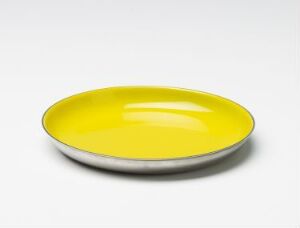  A shallow, round dish designed by Grete Prytz Kittelsen, crafted from stainless steel with a bright yellow enamel interior and a bare metallic edge, exemplifying modern Scandinavian design.