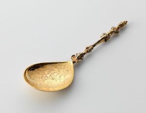  An intricately engraved and gilded silver spoon, with the title "Sølvskje," made by an unidentified artist. The spoon has a rich golden bowl with detailed engravings and a textured, ornate silver handle.