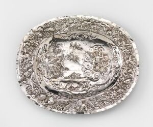  Ornate oval silver platter with embossed floral and scroll motifs, exhibiting intricate detail and varying shades of silver due to the polished and textured surfaces.