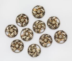  A set of ten ornate, golden floral-patterned circular objects, likely metal buttons or adornments, arranged in two neat rows on a light background. Each item features a central raised dome surrounded by intricate leaf-like designs.