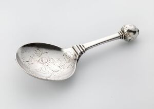  A polished silver spoon with etched floral patterns in the bowl and a spherical finial on the handle, lying on a smooth off-white to light grey gradient background. Artistname and title are unknown.