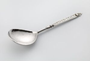  An antique silver spoon by Rasmus Gullsmed titled "Sølvskje," featuring a highly polished bowl and an ornately decorated handle with floral or ornamental designs, crafted using casting, chasing, and engraving techniques on silver. The spoon rests on a neutral background, displaying the reflective qualities of the silver material.