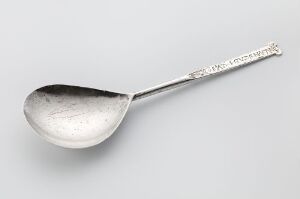  A silver spoon titled "Sølvskje" by an unidentified artist, featuring a slender, engraved handle and a gently worn bowl, against a neutral gray background.