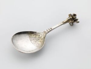  An antique gilded silver spoon, with engraved details and an ornate cluster of floral designs on the handle's finial, titled "Skje" by an unidentified artist, representing historic tableware design.