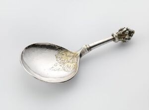  An antique silver spoon titled "Sølvskje" crafted from cast, wrought, engraved, and partly gilded silver, featuring intricate engravings near the bowl and a decorative clustered finial on the handle, resting against a neutral background. Artist unidentified.