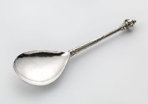  Antique silver spoon titled "Skje" by an unidentified artist, featuring an oval bowl and an intricately engraved handle, showcasing the lustrous quality of forged and cast silver against a plain background.