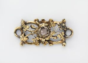  An antique gold brooch with a central smoky quartz gemstone, surrounded by detailed goldwork mimicking natural and floral shapes, set against a light grey background.