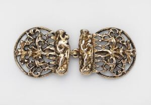  An intricate golden filigree object, possibly a piece of antique jewelry, featuring a symmetrical lace-like design, is displayed against a neutral light gray background.