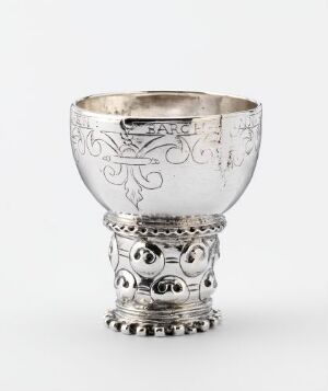  An ornate silver drinking vessel titled "Drikkebeger" by an unidentified artist, featuring intricate engraved and raised designs with an interior gilding, set against a plain background. The cup demonstrates complex craftsmanship, with a decorative base and a smoother upper bowl