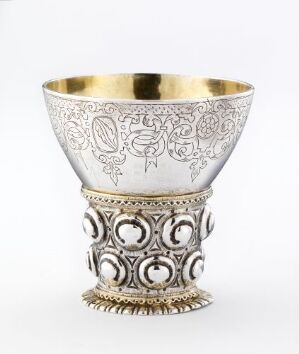  A decorative metal cup with an intricate silver exterior featuring engraved and raised patterns, and a golden interior lining, set against a light grey background.