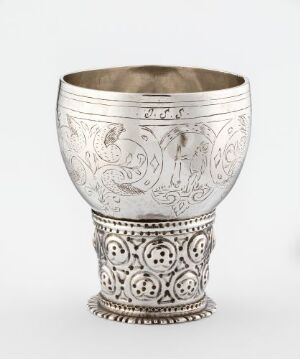  An ornate silver cup with engraved designs featuring flora, fauna, or mythical creatures on its body and a decorative base with medallion-like patterns. The cup has a slightly conical shape and is displayed against a neutral background.