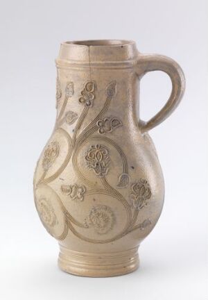  A beige ceramic pitcher with a curvy form and embossed scroll and floral designs, featuring a large handle on the side, set against a neutral background.