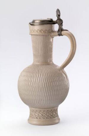  An off-white ceramic jug with a textured diamond pattern and a metallic lid set against a light background.