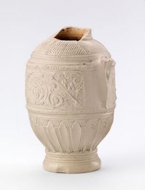  A cream-colored ceramic vessel, likely an ancient amphora or urn, features intricate embossed decorations including acanthus leaves and geometric patterns, with the top portion broken off. It is displayed against a light gray background.