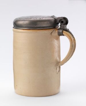  A traditional creamy beige stoneware beer stein with a curved handle and pewter lid, showcasing a classic, rustic design.