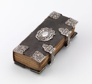  An antique book with dark cover and intricate silver decorations on the corners and center, set against a light gray background.